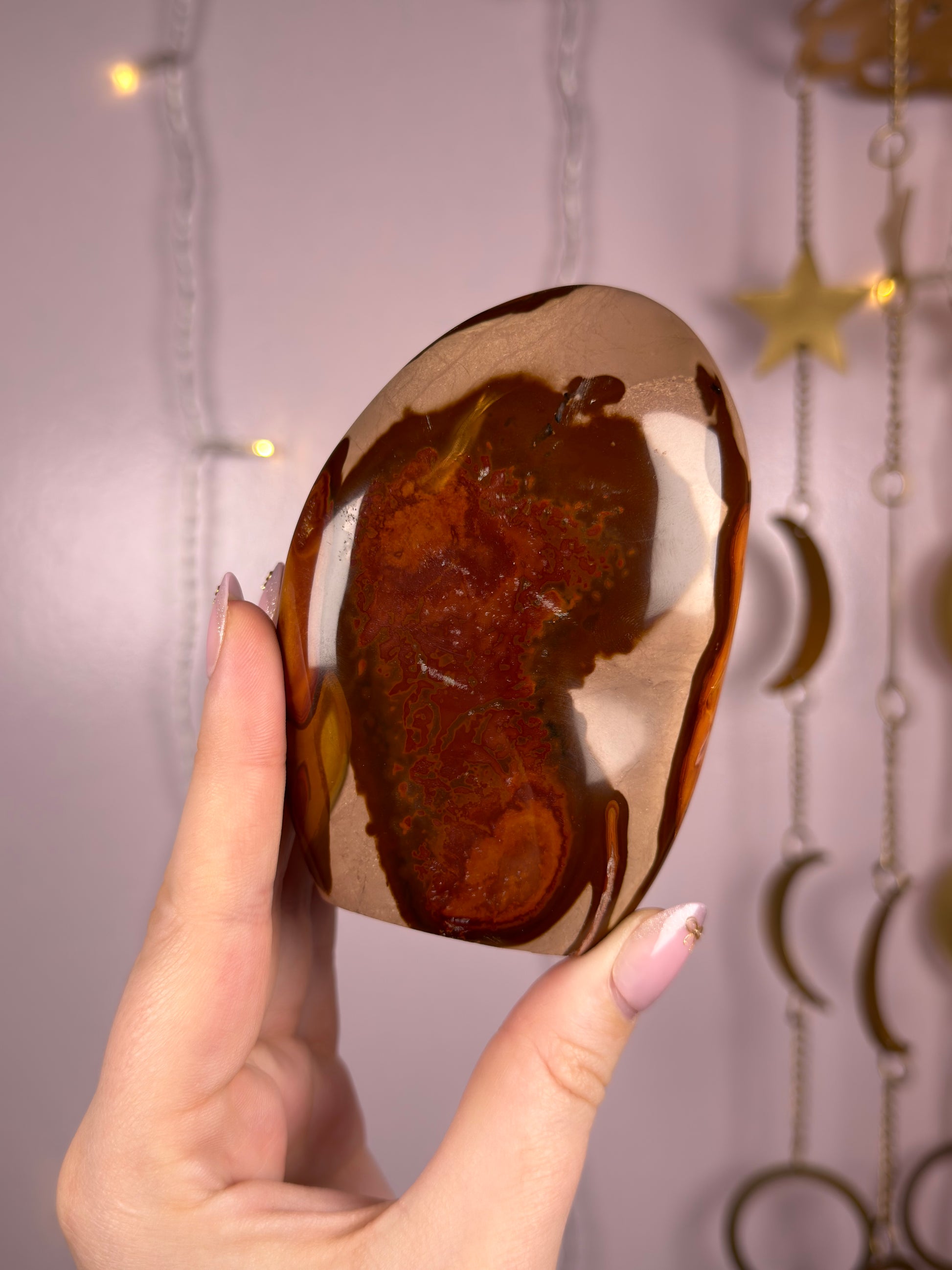 Red, brown and orange polychrome jasper crystal held with a hand in front of fairy lights. 